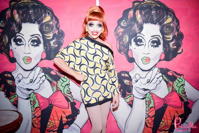 Bianca del Rio in Rio posing in front of her portraits by Suriani.